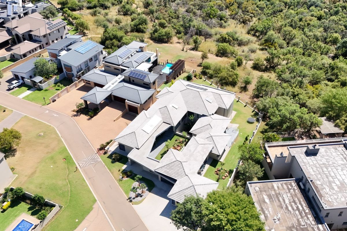 Aerial view of a modern residential property featuring a tiled roof, solar panels, paved driveway, and a private swimming pool within a landscaped estate.