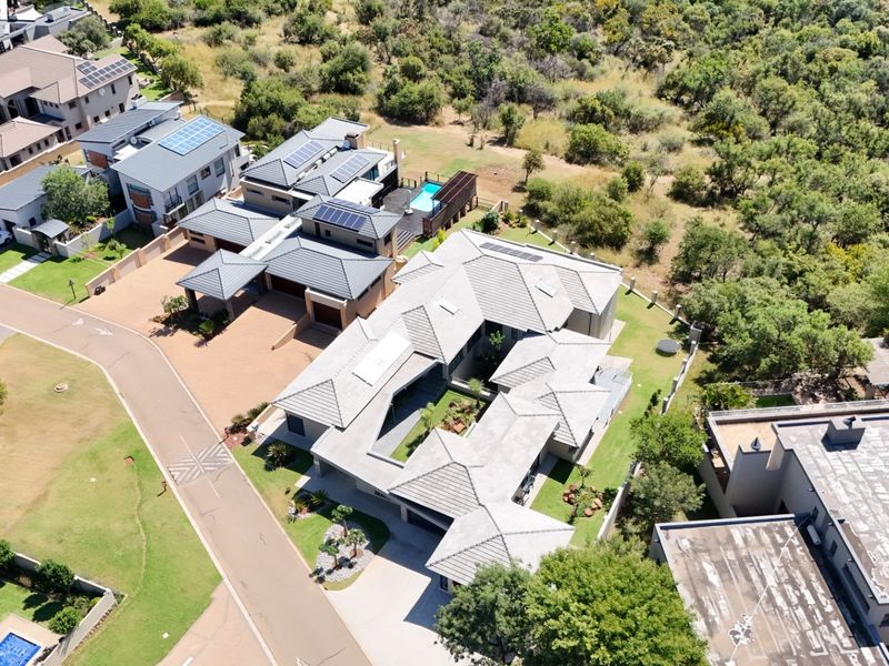 Aerial view of a modern residential property featuring a tiled roof, solar panels, paved driveway, and a private swimming pool within a landscaped estate.