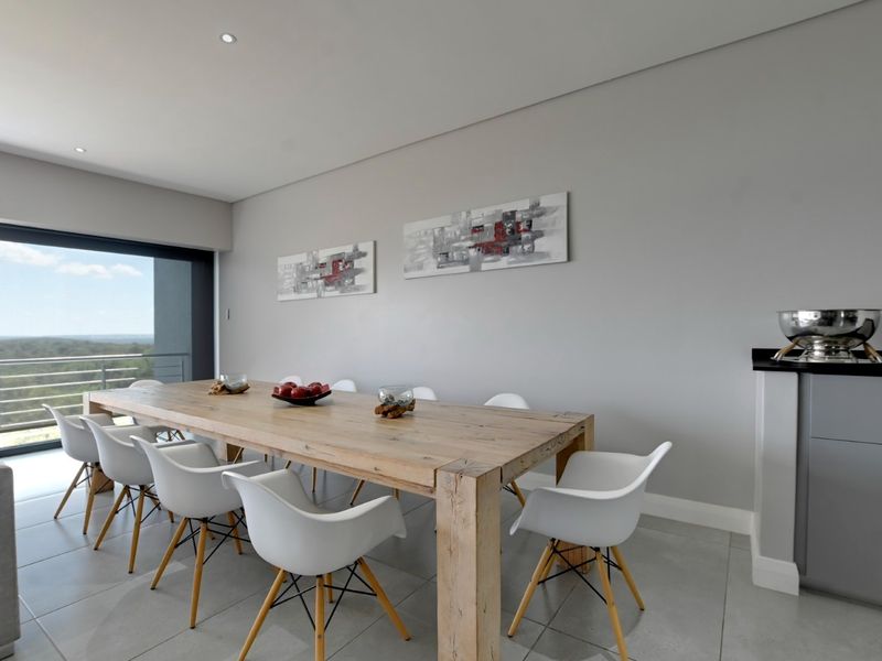 Modern dining area featuring large format floor tiles, recessed lighting, and a sliding glass door providing access to an outdoor balcony with scenic views.