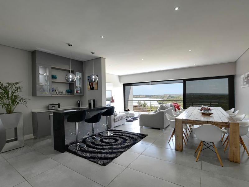 Spacious open-plan living and dining area featuring a modern built-in bar, sleek tiled flooring, and large sliding doors opening to a scenic outdoor view.