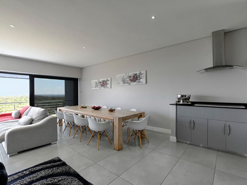Spacious open-plan living and dining area featuring large format floor tiles, recessed lighting, and a modern kitchenette with built-in cabinetry and extractor fan.