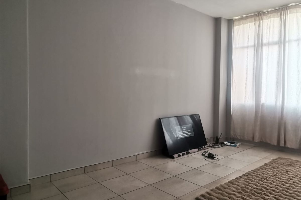 A bright, empty living room featuring neutral tiled flooring and a large window, offering a blank canvas for personalization.