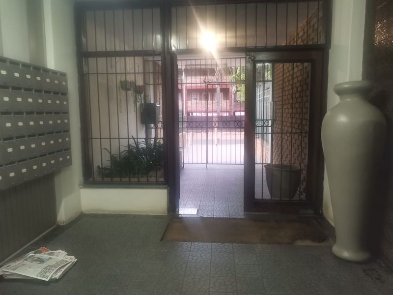 A secure apartment building entrance lobby featuring tiled flooring, a bank of metal mailboxes, and a security gate leading to the exterior.
