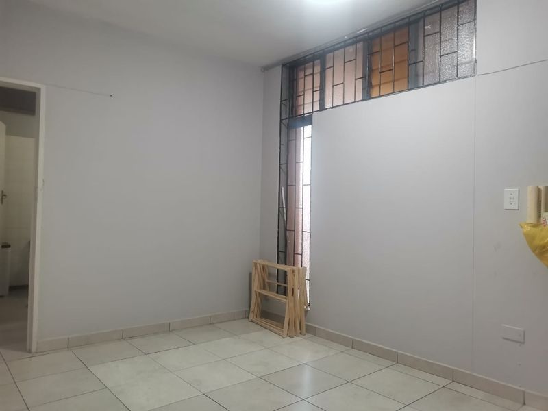An empty bedroom featuring neutral tiled flooring and security bars on the window, offering a blank canvas for personalization.