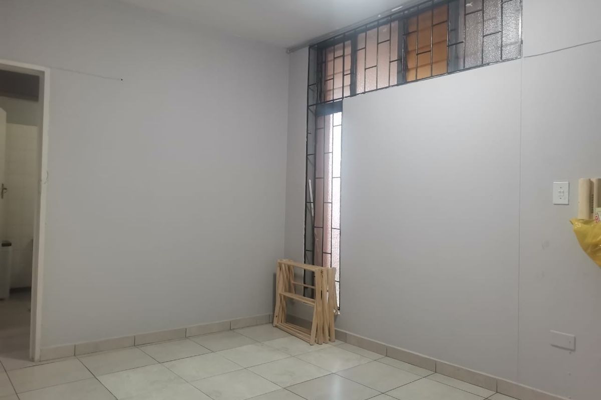 An empty bedroom featuring neutral tiled flooring and security bars on the window, offering a blank canvas for personalization.