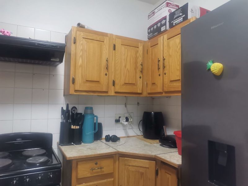 A functional kitchen featuring traditional wooden cabinetry, laminate countertops, ceramic wall tiling, and a built-in electric stove with an extractor fan.