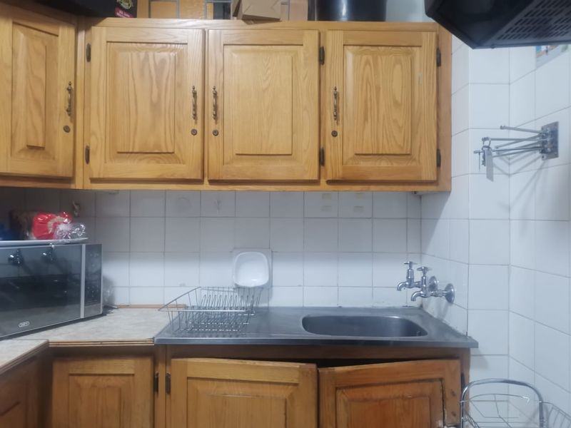 A functional kitchen area featuring traditional wooden cabinetry, a stainless steel sink with wall-mounted taps, and a tiled backsplash.