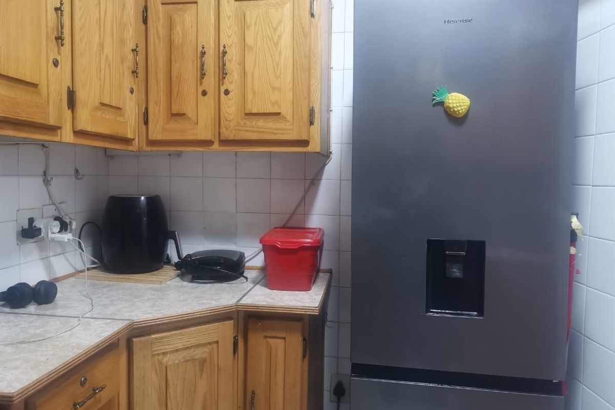 A functional kitchen area featuring traditional wooden cabinetry, laminate countertops, and a tiled backsplash, offering potential for a modern cosmetic update.