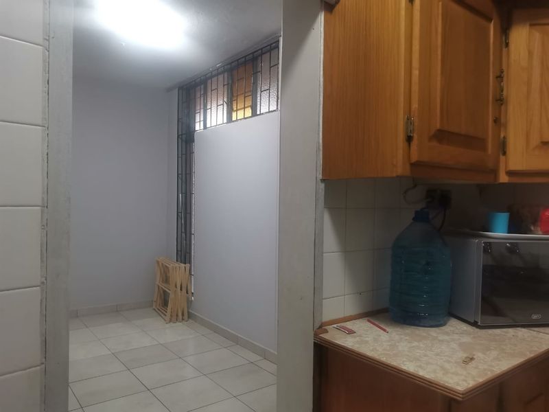 A functional kitchen area featuring wooden cabinetry, tiled backsplash, and tiled flooring, adjacent to a secondary utility space with security bars on the window.
