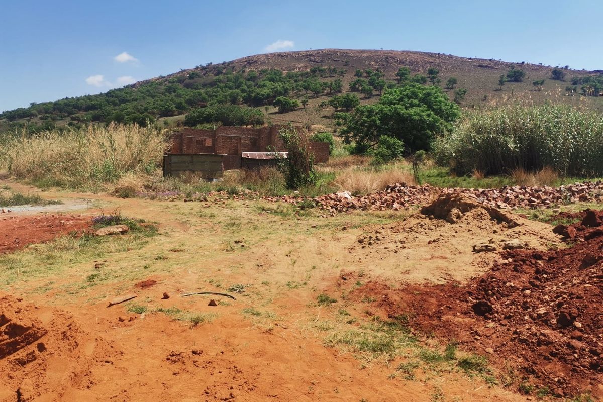 A view of an undeveloped residential plot featuring natural terrain, hillside backdrop, and scattered construction debris on the site.