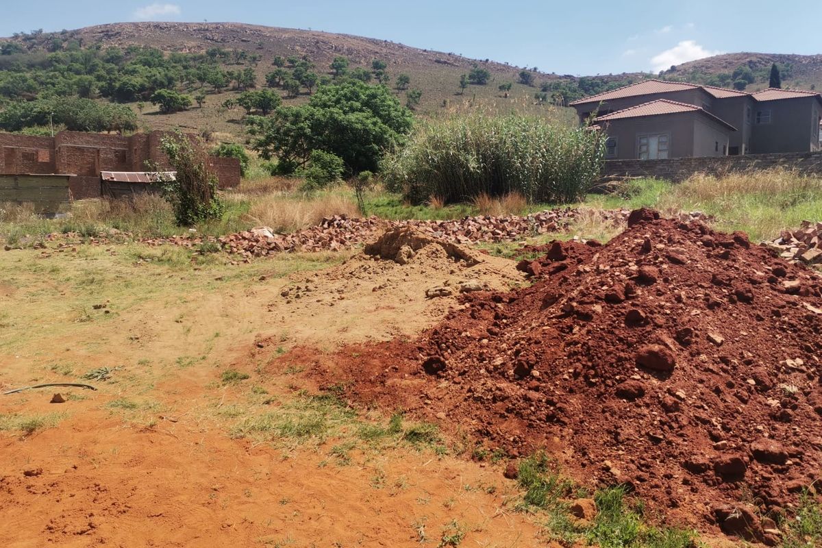 A view of the vacant residential plot featuring unimproved soil, piles of rubble, and a partially constructed brick structure in the background.