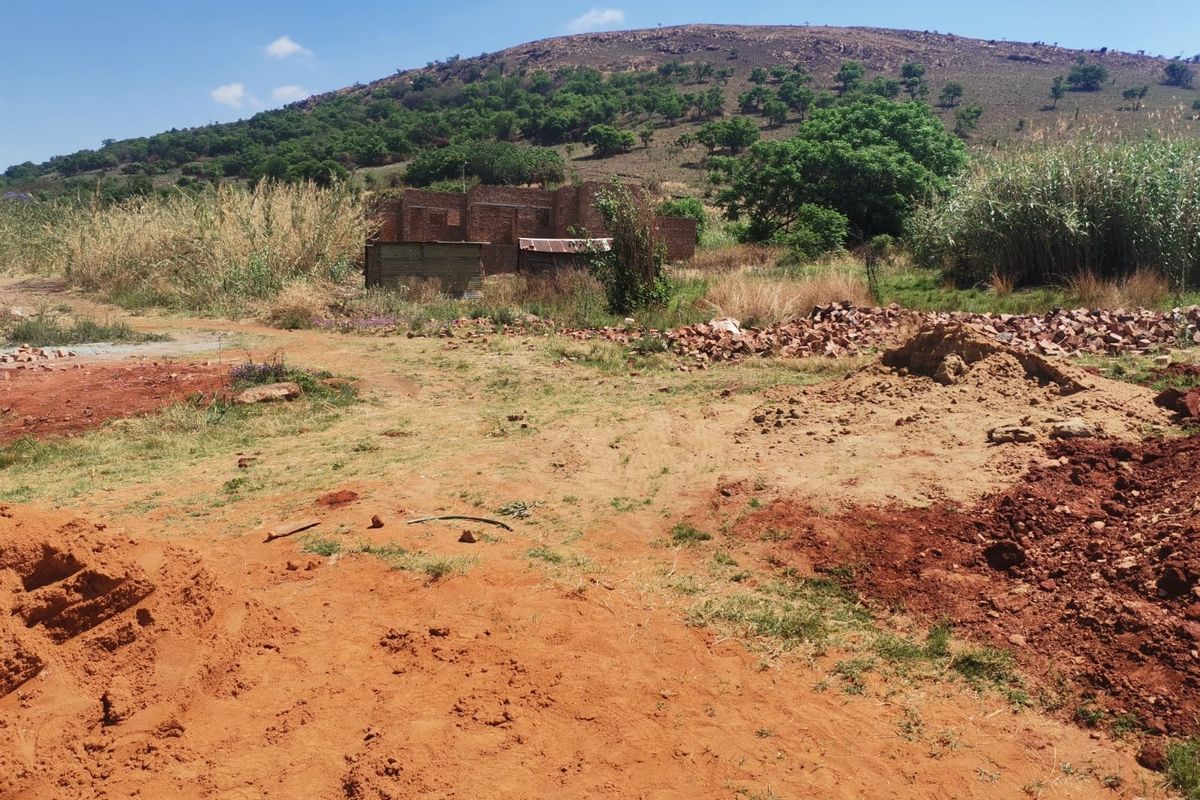 Vacant residential land featuring an unfinished brick structure and natural landscape with mountain views.