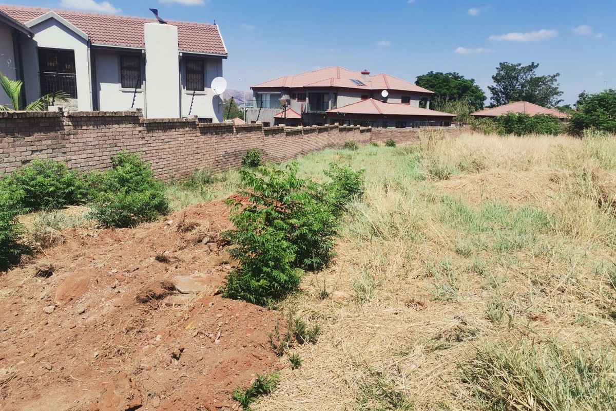 A view of a vacant residential plot featuring a brick boundary wall and surrounding established residential properties.