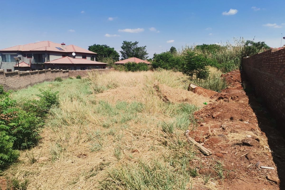 A vacant residential plot featuring overgrown grass and enclosed by perimeter brick walls, offering a blank canvas for future development.