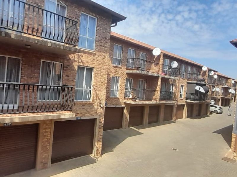 Exterior view of a multi-story apartment complex featuring face-brick facade, private balconies with metal railings, and ground-level garage access.