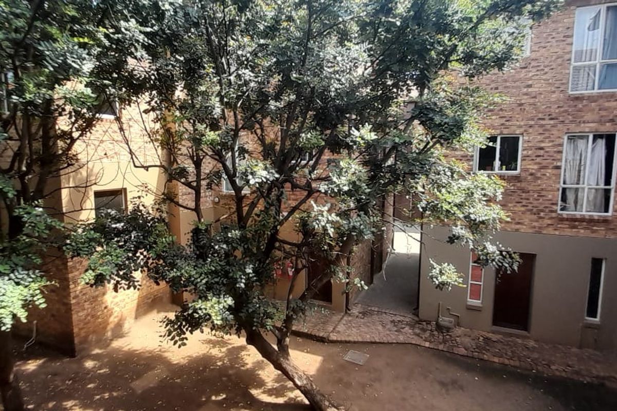 A view of the apartment complex rear courtyard featuring face-brick exterior walls, paved ground area, and established trees.