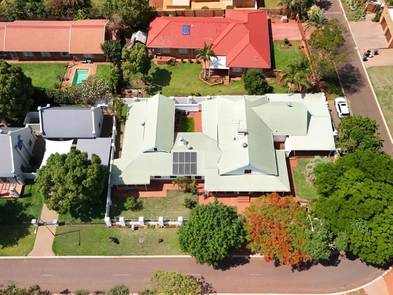 Aerial view of a residential property featuring a metal roof, installed solar panels, a well-maintained garden, and a paved driveway within a suburban setting.
