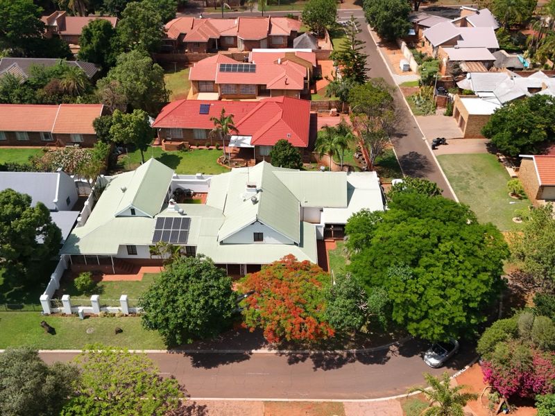 Aerial view of a residential property featuring a metal roof with solar panels, a well-maintained garden, and a paved driveway in a suburban setting.