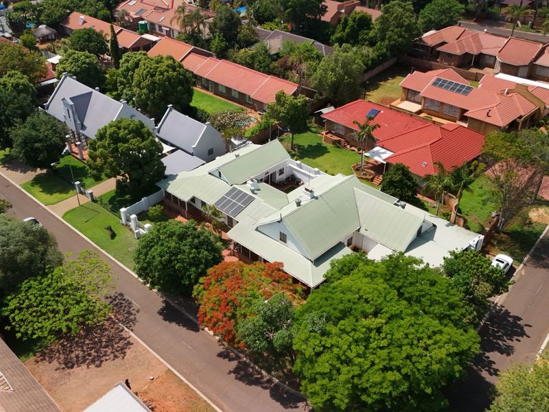 Aerial view of a residential property featuring a pitched roof with solar panels, surrounded by established trees and a well-maintained garden in a suburban neighborhood.