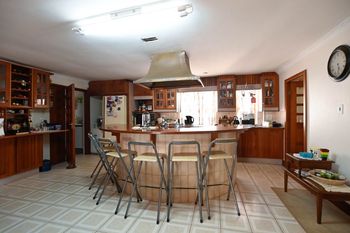 Spacious kitchen featuring wooden cabinetry, a central tiled island with a breakfast bar, and a stainless steel extractor hood.