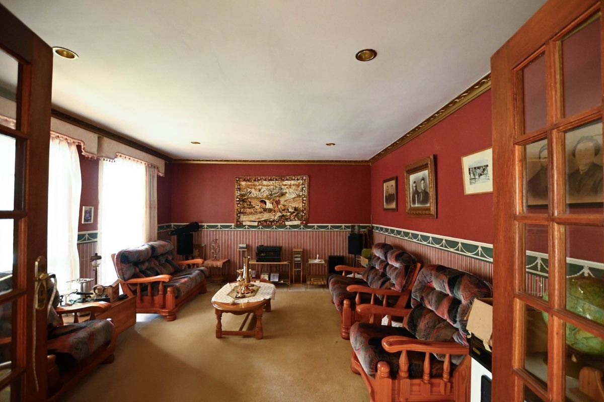 A traditional living room featuring decorative crown molding, recessed lighting, and classic french door entry, currently finished with dated wall treatments and carpeting.
