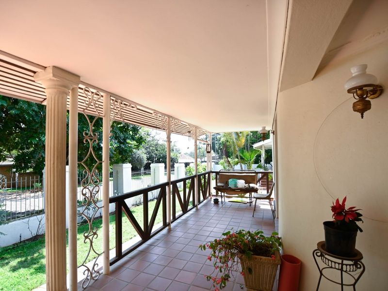 A covered patio featuring tiled flooring, decorative columns, and a wrought iron balustrade overlooking the garden.