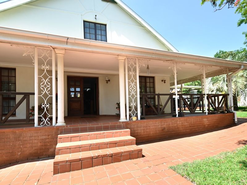 A charming front facade featuring a spacious covered veranda with classic wrought iron columns, brick steps, and timber-framed doors and windows.