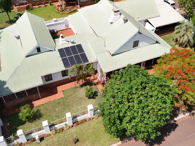 Aerial view of a residential property featuring a corrugated metal roof with installed solar panels, surrounding garden, and paved patio area.