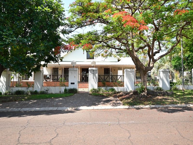 Front elevation of a house featuring a covered veranda, secure gated entrance with wrought iron fencing, and mature landscaping.