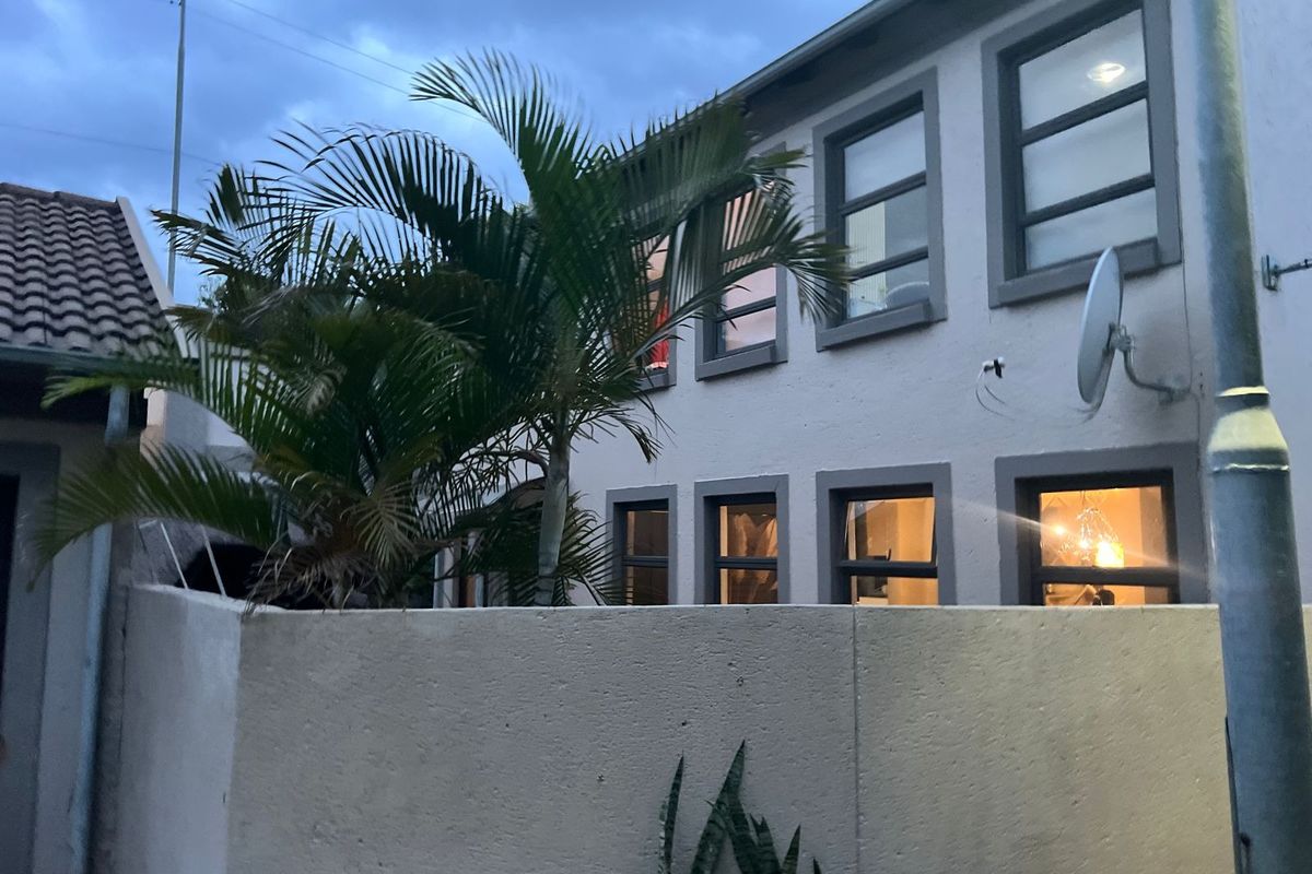 A view of the rear exterior of the townhouse, featuring a boundary wall, established palm tree, and multiple windows.