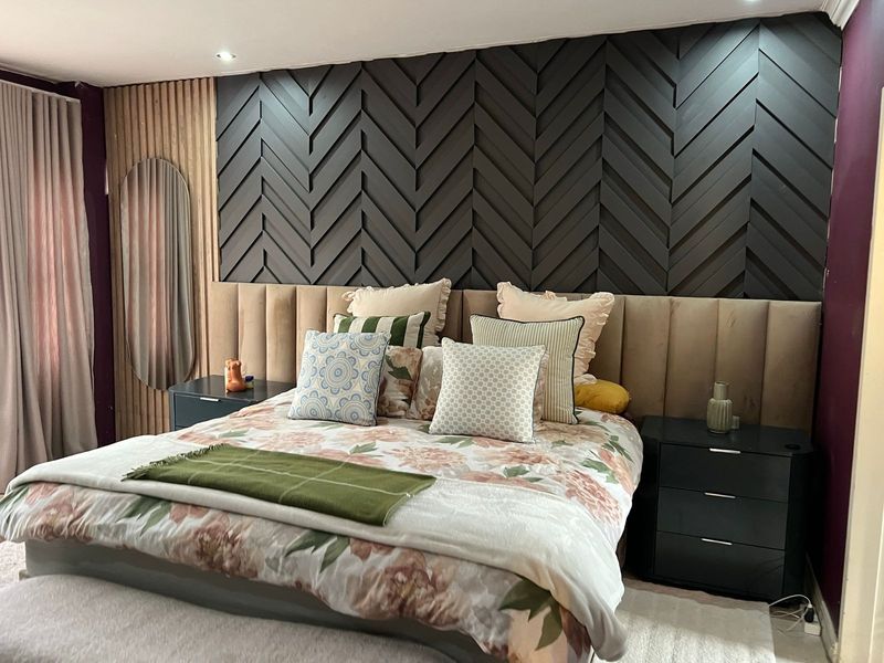 A well-appointed bedroom featuring a striking dark chevron feature wall, integrated slatted wood paneling, and a custom upholstered headboard with recessed lighting.
