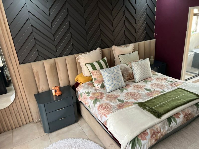 A well-appointed bedroom featuring a large upholstered headboard and a decorative dark herringbone feature wall, with tiled flooring throughout.