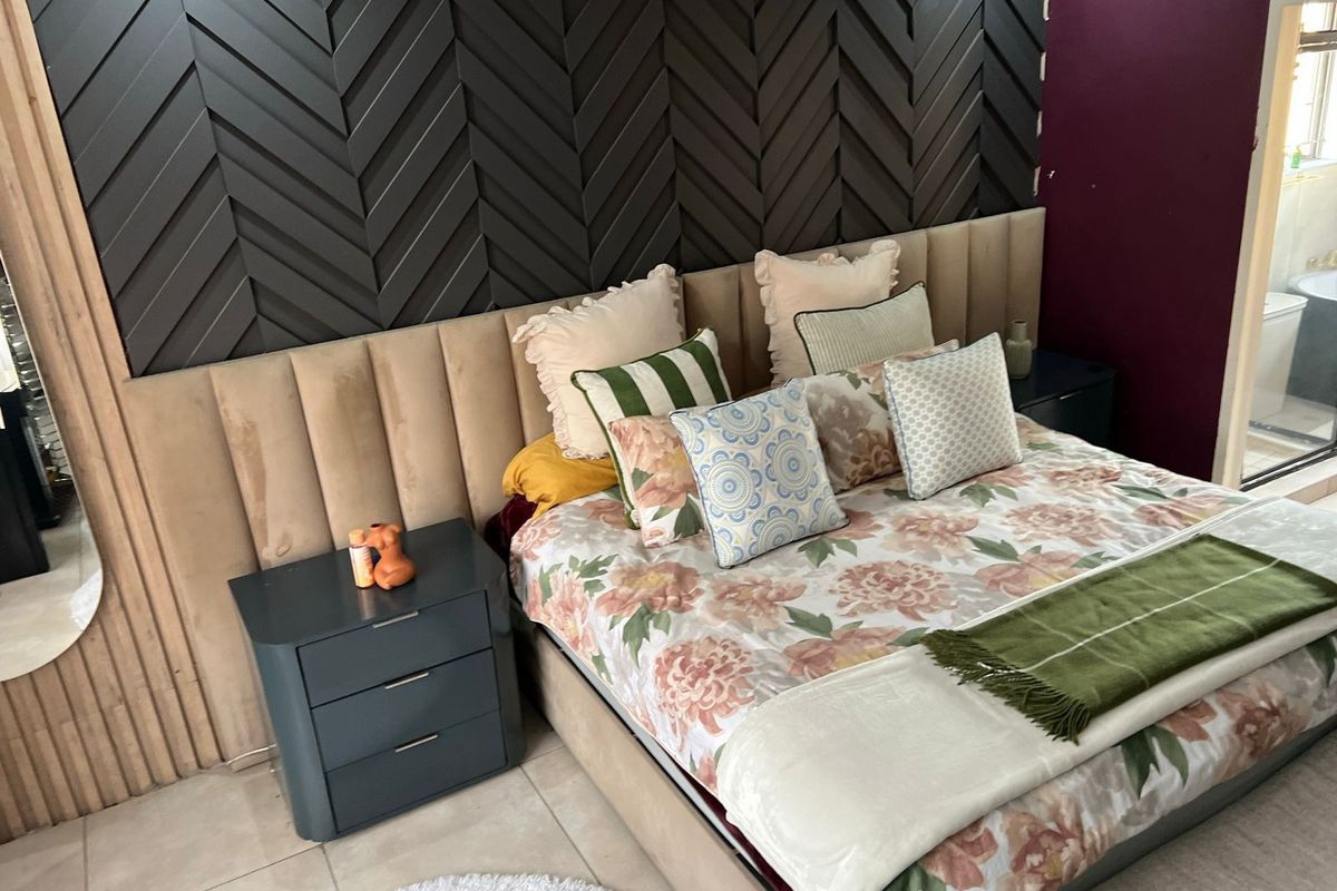 A well-appointed bedroom featuring a large upholstered headboard and a decorative dark herringbone feature wall, with tiled flooring throughout.
