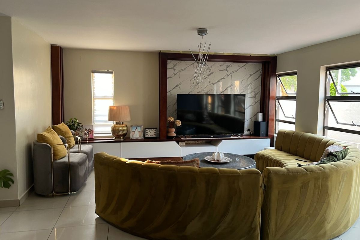 Spacious living room featuring a modern built-in media unit with marble-effect paneling, large tiled floors, and ample natural light from multiple casement windows.