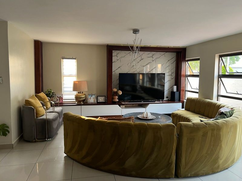 Spacious living room featuring a modern built-in media unit with marble-effect paneling, large tiled floors, and ample natural light from multiple casement windows.