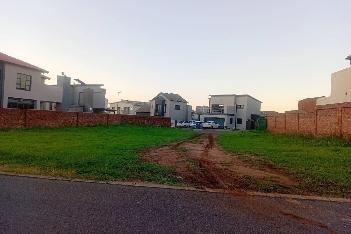 A vacant residential plot featuring a grass lawn and brick boundary walls, situated in a developed neighborhood with street access.