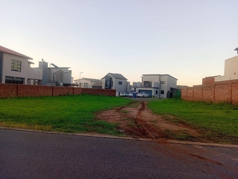 A vacant residential plot featuring a grass lawn and brick boundary walls, situated in a developed neighborhood with street access.
