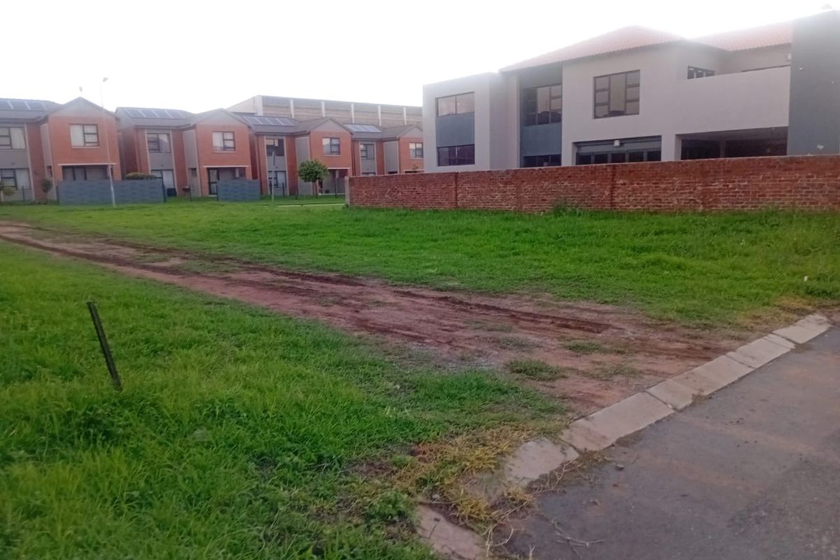 A vacant residential plot featuring a grass lawn and brick boundary wall, situated in a developed neighborhood setting.