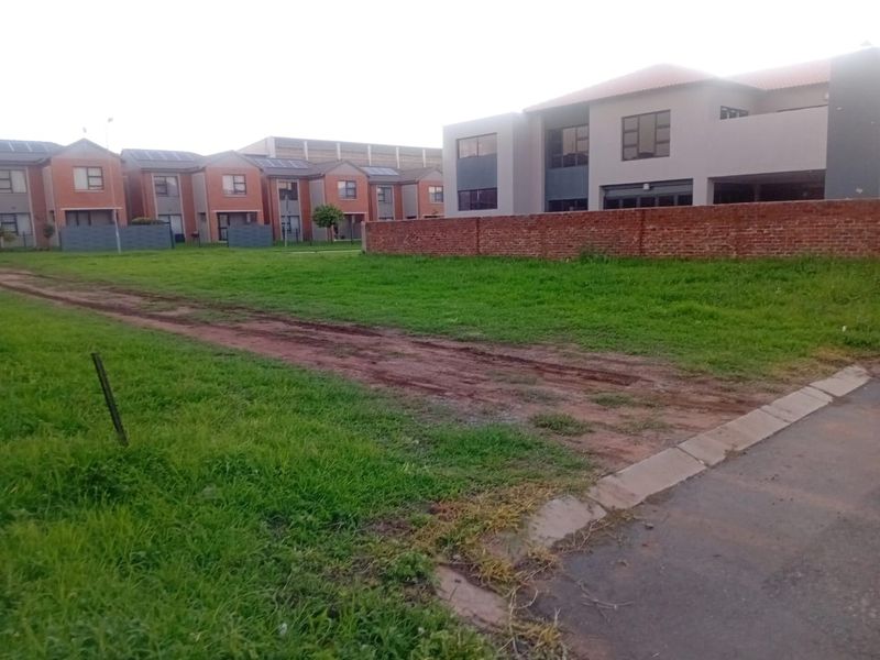 A vacant residential plot featuring a grass lawn and brick boundary wall, situated in a developed neighborhood setting.