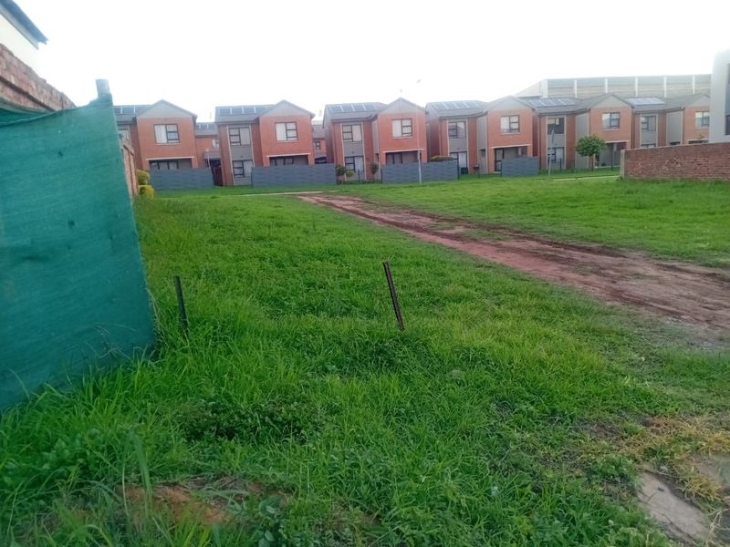 A vacant residential plot featuring a grass lawn and dirt driveway, situated in a developed residential estate.