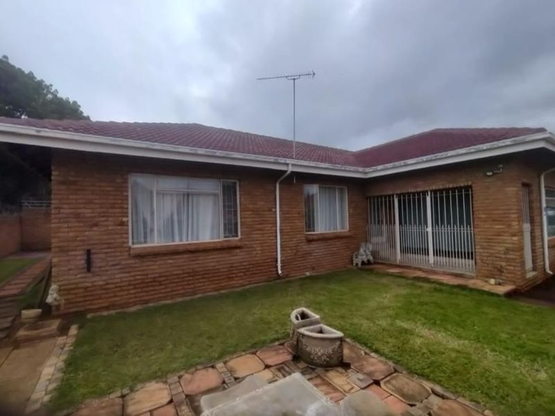 Rear view of a face brick house featuring a tiled roof, security bars on windows and doors, and a paved patio area.