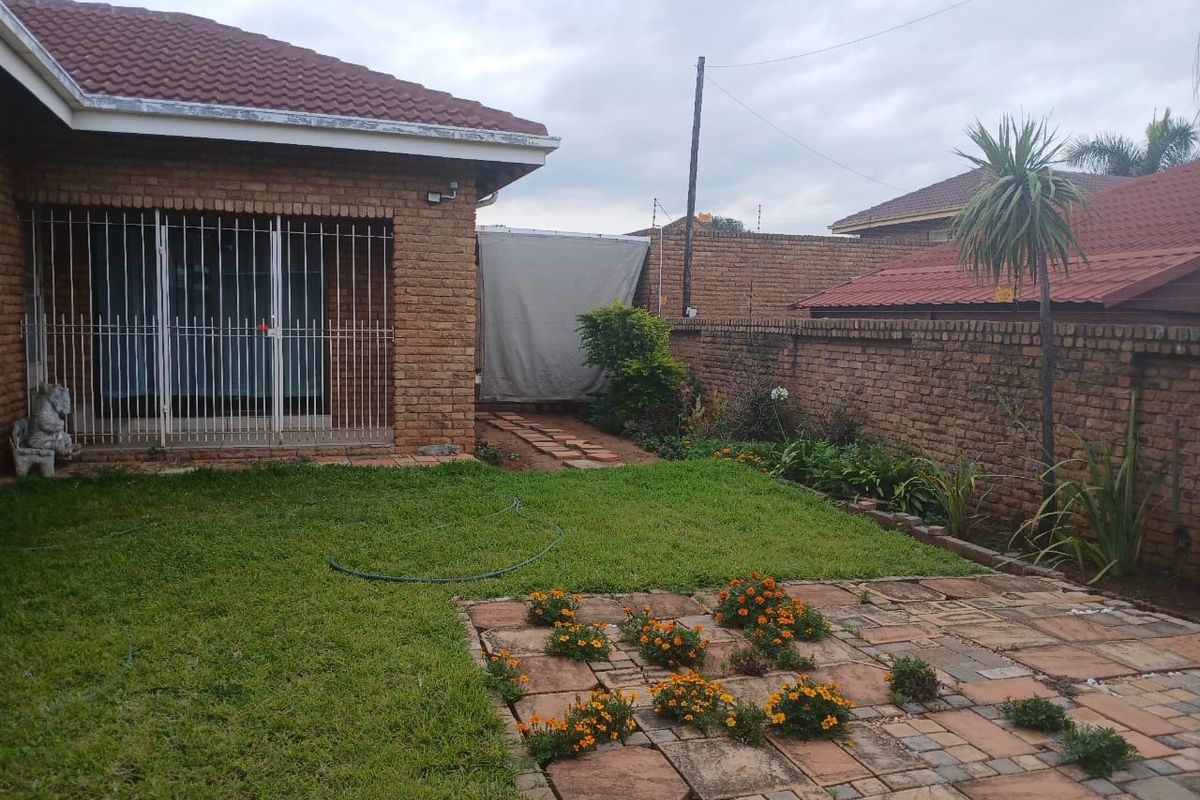 A rear garden view featuring a brick-walled perimeter, a small lawn, and a paved patio area adjacent to the main house structure.