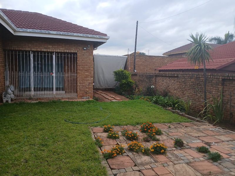 A rear garden view featuring a brick-walled perimeter, a small lawn, and a paved patio area adjacent to the main house structure.