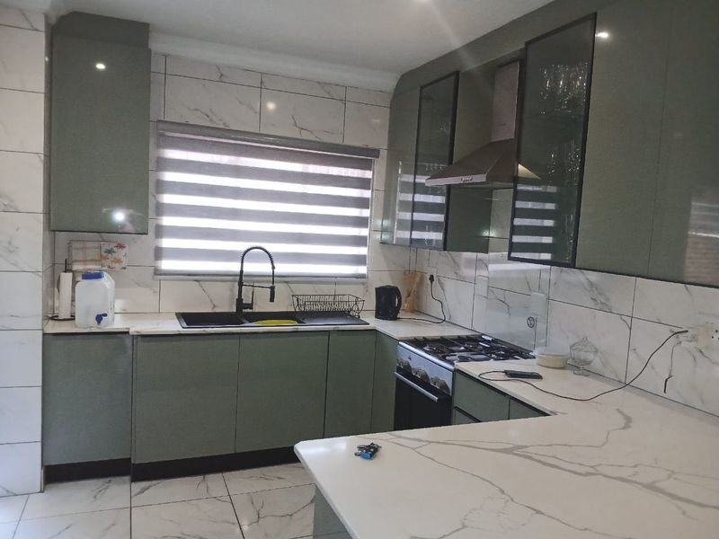 Modern kitchen featuring sage green cabinetry, marble-look tiled walls and floors, quartz countertops, and high-quality built-in appliances.