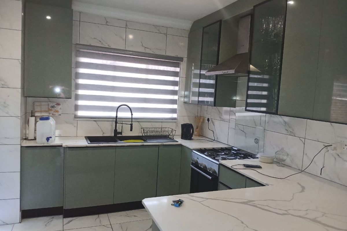 Modern kitchen featuring sage green cabinetry, marble-look tiled walls and floors, quartz countertops, and high-quality built-in appliances.