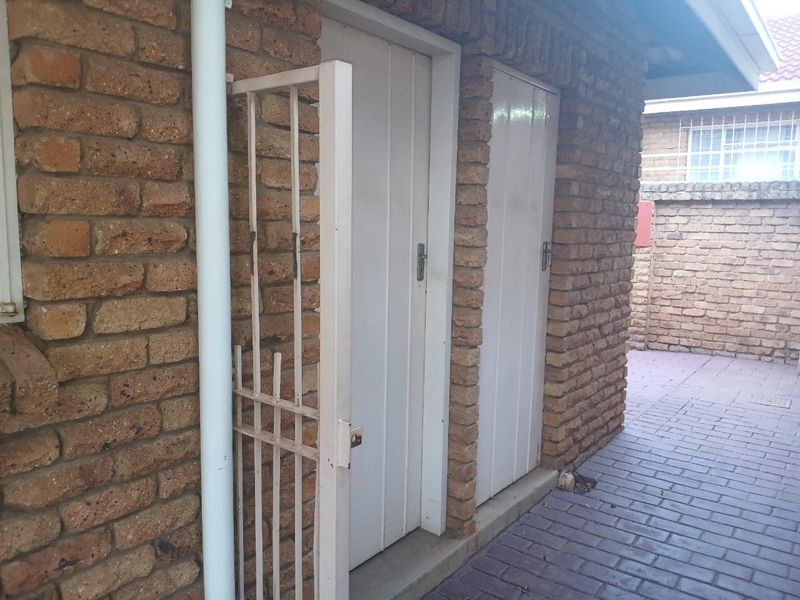 Exterior view of the rear of the property featuring face brick walls, paved pathways, and secure access doors.