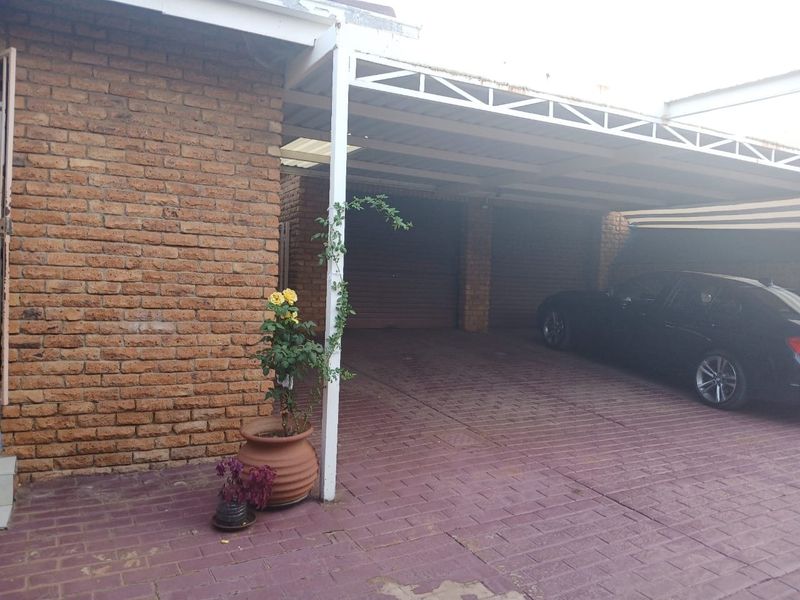 A covered carport area with brick exterior walls and paved driveway, providing sheltered parking space.