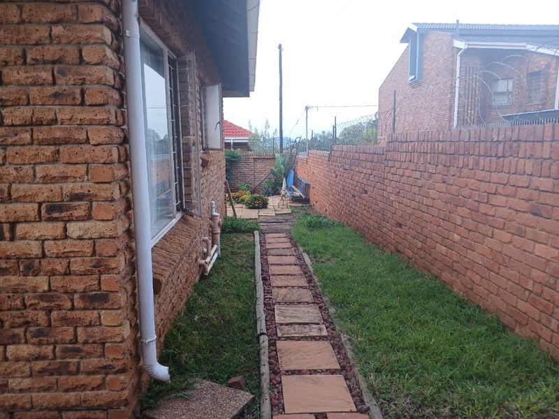 A side garden path featuring face brick walls, a paved walkway, and a boundary wall, offering potential for landscaping improvements.