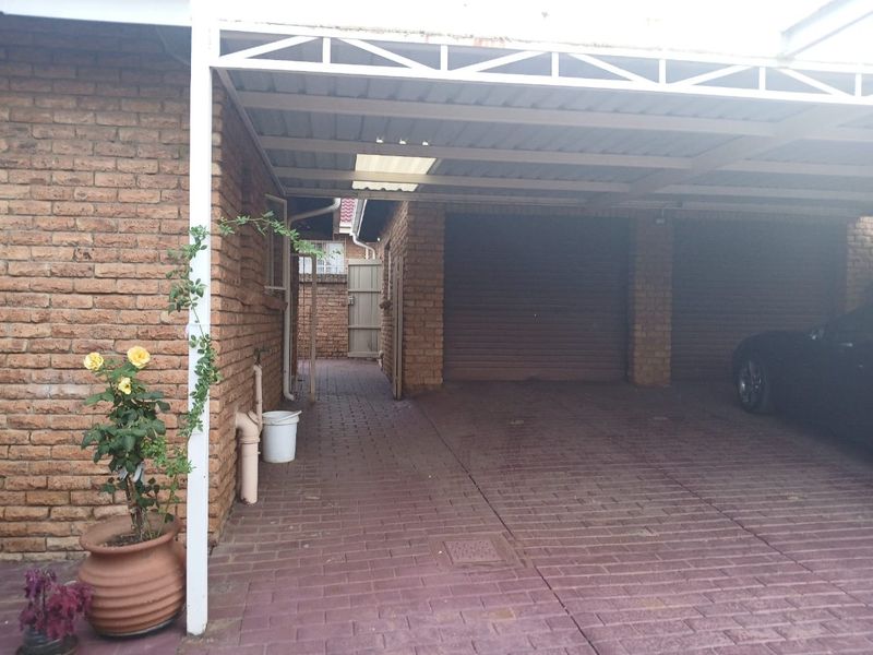 A covered carport area with brick walls and paved flooring, providing sheltered parking space for vehicles.
