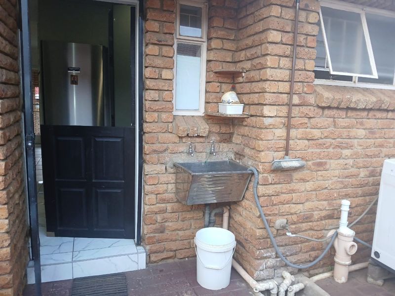 Exterior laundry area featuring a stainless steel utility sink, exposed brick wall, and plumbing connections for washing equipment.